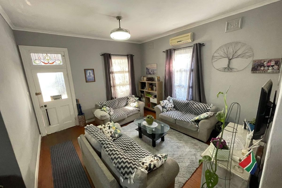 A comfortable living room featuring timber flooring, a split-system air conditioner, and a classic front door with leaded glass detailing.