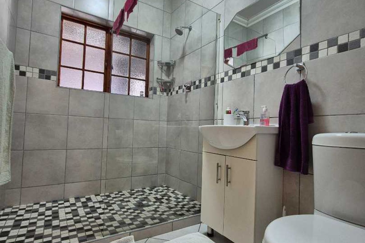 A functional bathroom featuring a walk-in shower with glass screen, vanity basin, and modern grey wall tiling with a decorative mosaic border.