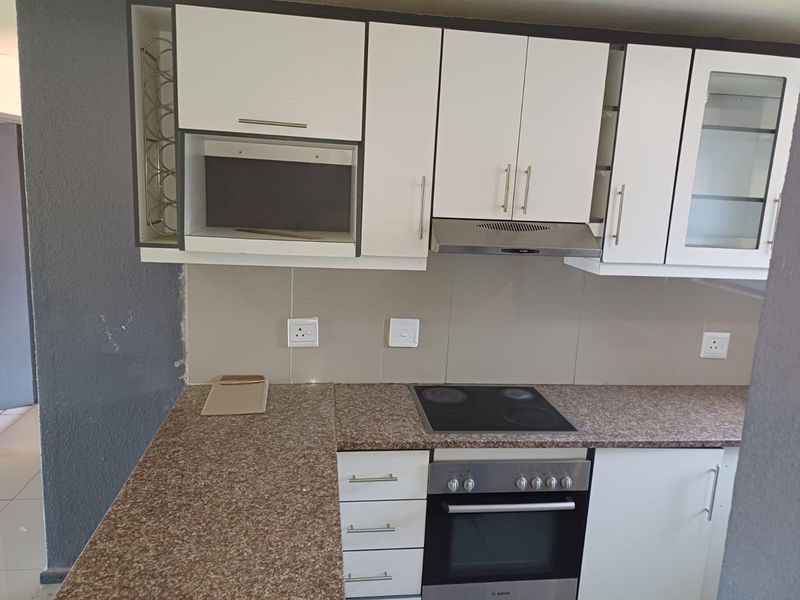 A functional kitchen featuring white cabinetry, a granite-look laminate countertop, built-in electric oven, hob, and extractor fan with a tiled backsplash.