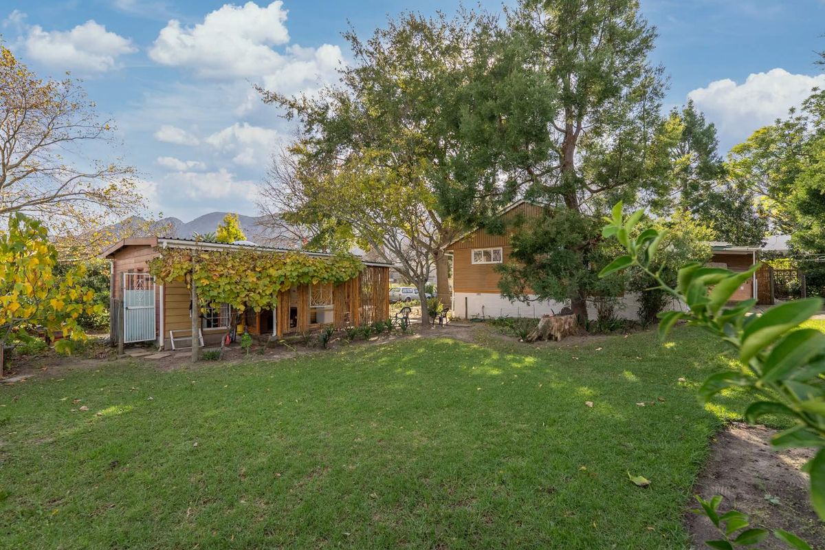 A spacious rear garden featuring a lawn, mature trees, and a timber-clad structure with an attached pergola.