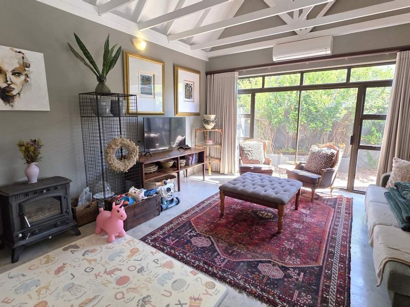A bright living room featuring a vaulted ceiling with exposed beams, polished concrete floors, a cast iron fireplace, and large sliding doors to the garden.
