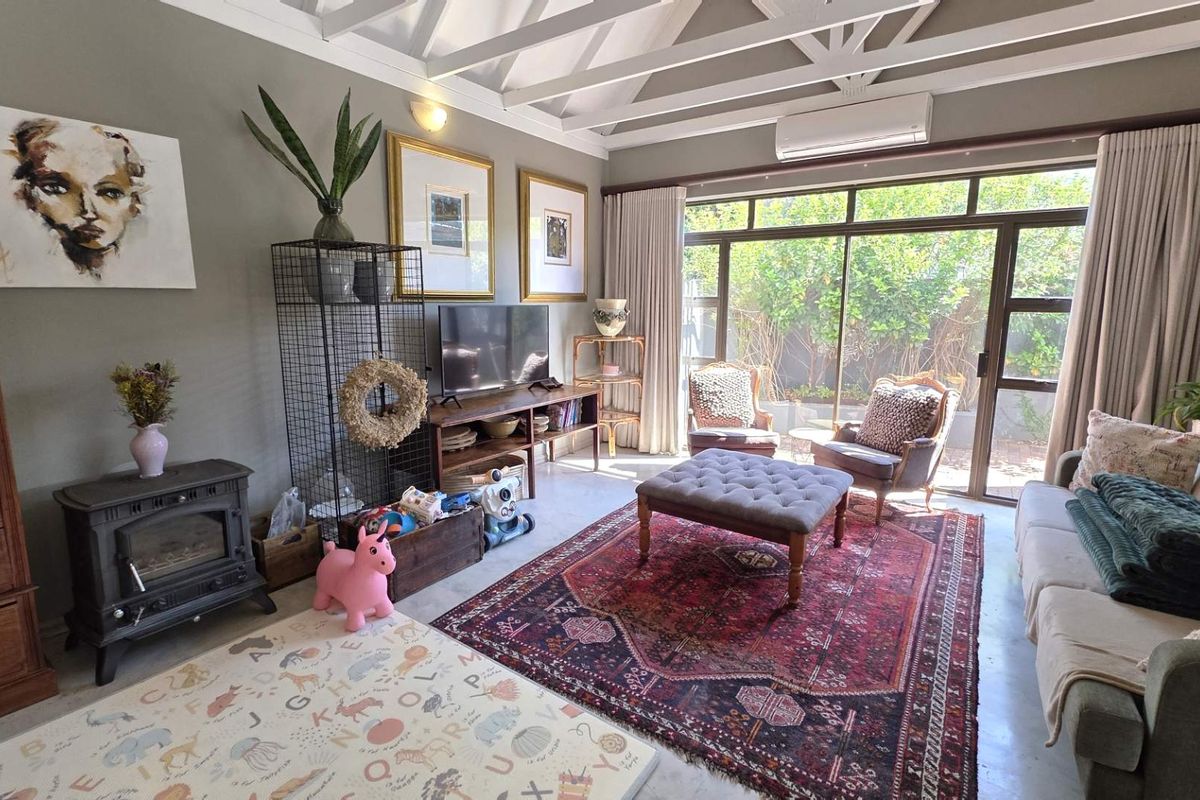 A bright living room featuring a vaulted ceiling with exposed beams, polished concrete floors, a cast iron fireplace, and large sliding doors to the garden.