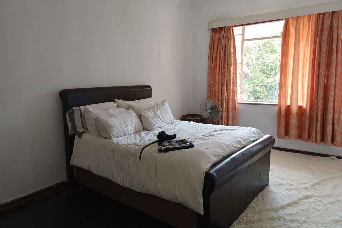 A bedroom featuring a large window with natural light, neutral walls, and dark flooring.