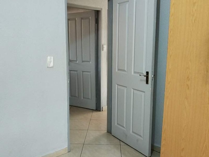A clean, tiled hallway featuring neutral grey walls and panelled interior doors leading to adjacent rooms.