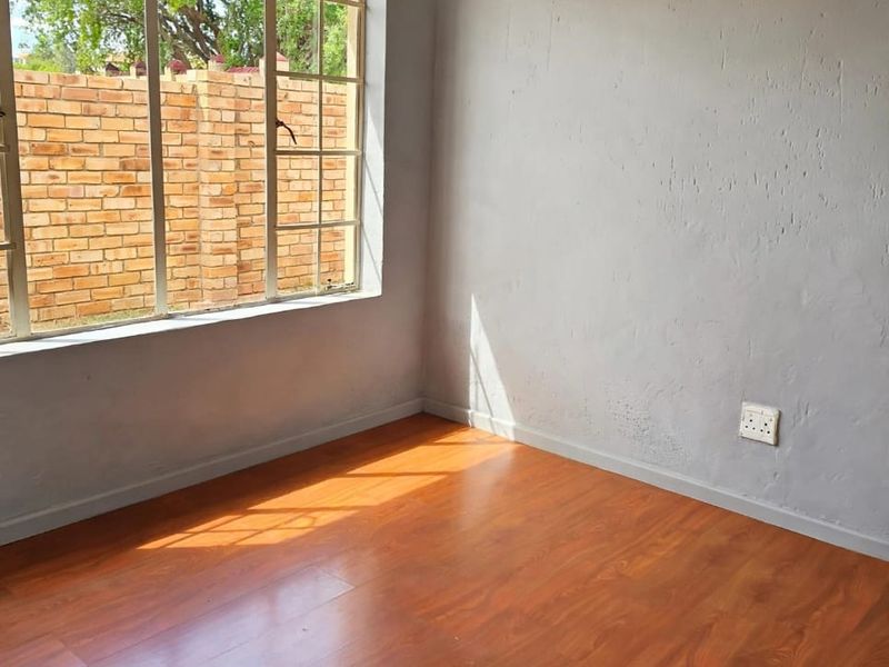 A bright, empty bedroom featuring laminate flooring, a large window, and neutral grey walls, offering a blank canvas for personalization.