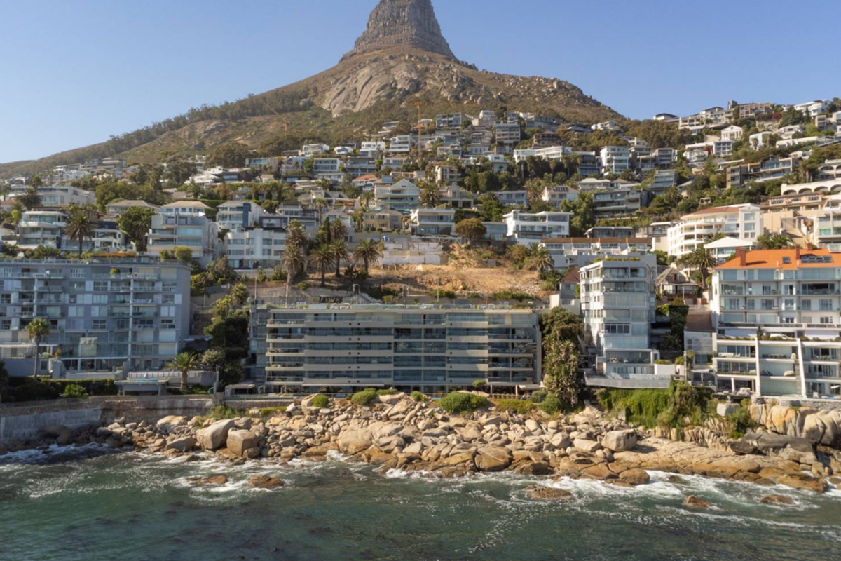 Aerial view of a coastal residential area featuring multi-story apartment buildings situated against a prominent mountain backdrop.