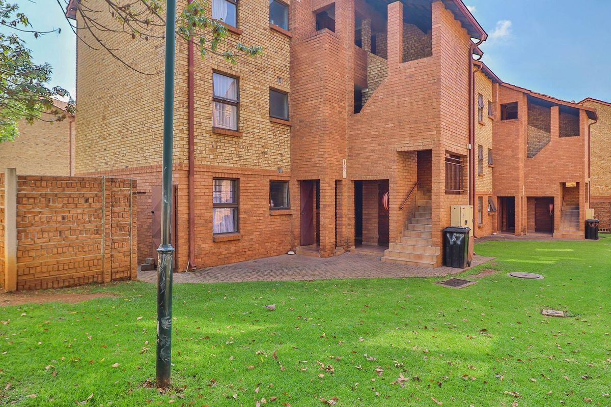 Exterior view of a multi-story apartment complex featuring face-brick facade, communal lawn area, and paved access paths.