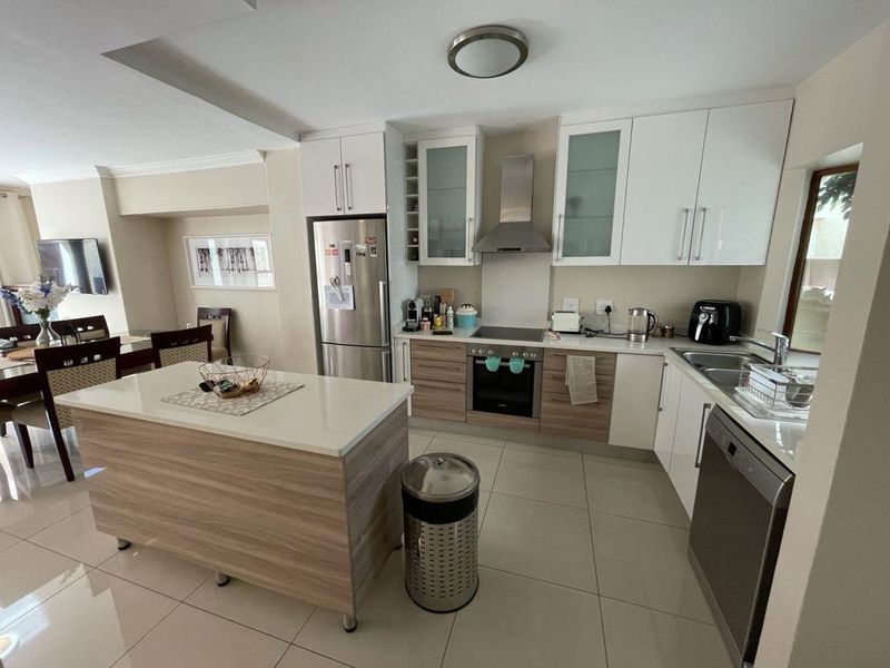 Modern open-plan kitchen featuring a central island, sleek cabinetry, built-in appliances, and tiled flooring, seamlessly flowing into the adjacent dining area.