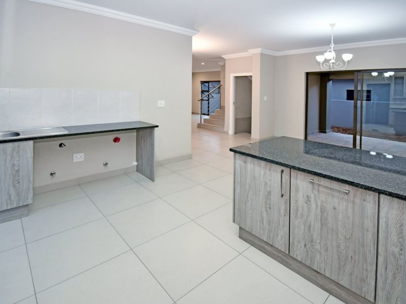 Modern kitchen featuring granite countertops, wood-grain cabinetry, and tiled flooring, with an open-plan layout leading to an outdoor patio area.