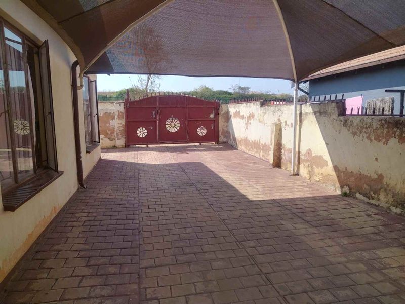 A paved outdoor area featuring a shade sail, metal gate, and boundary wall, providing a functional space for parking or outdoor use.