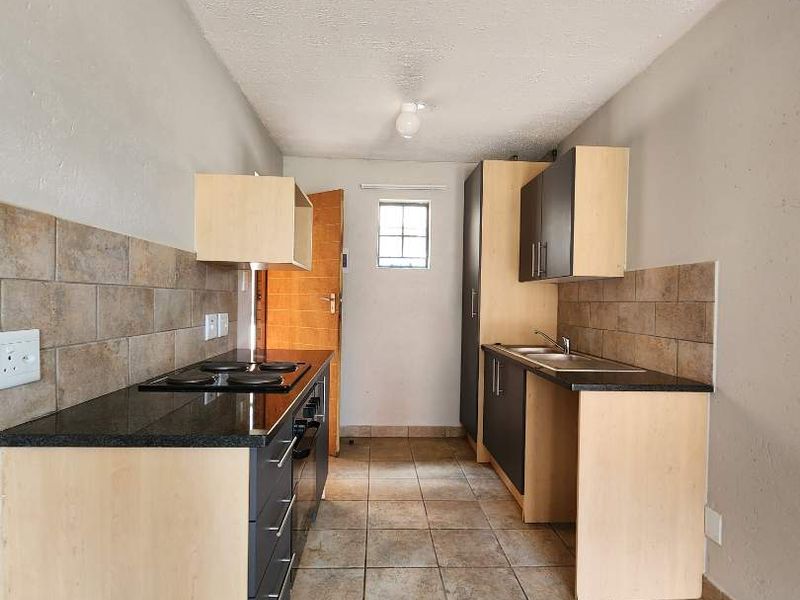 A functional galley-style kitchen featuring built-in cabinetry, granite countertops, a ceramic tile backsplash, and tiled flooring.