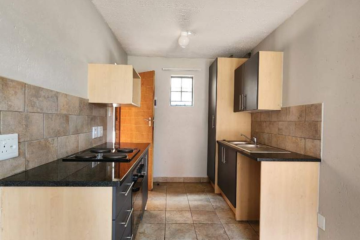 A functional galley-style kitchen featuring built-in cabinetry, granite countertops, a ceramic tile backsplash, and tiled flooring.