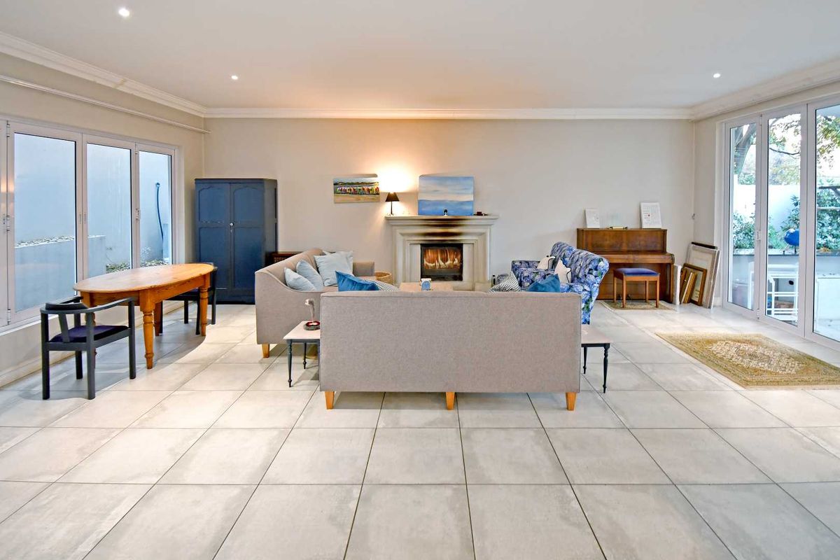 Spacious living room featuring large format floor tiles, a central fireplace, and dual sets of glass doors providing access to outdoor areas.