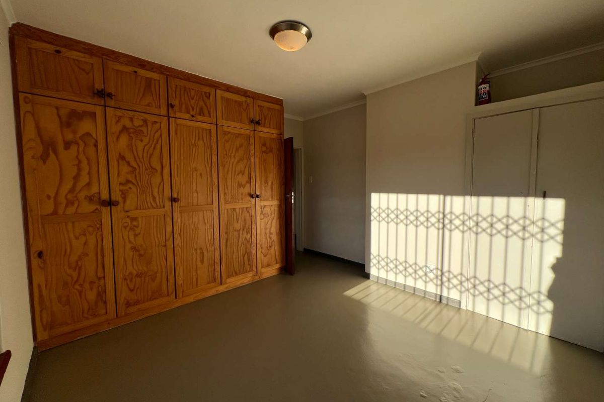A spacious bedroom featuring extensive built-in wooden cabinetry, a security gate on the window, and neutral wall finishes.