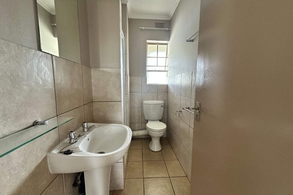 A functional bathroom featuring a pedestal basin, toilet, and tiled walls with a neutral color palette.