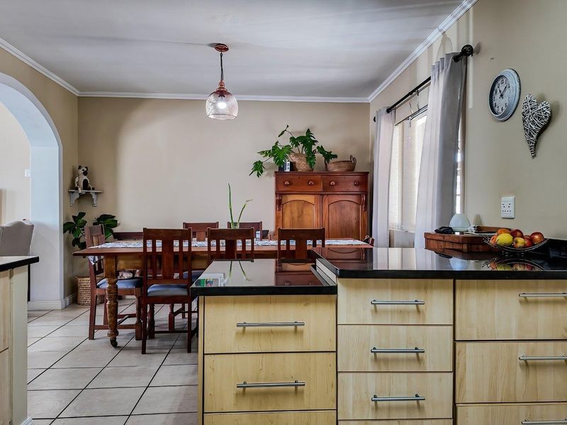 Open-plan kitchen and dining area featuring light-wood cabinetry, black granite countertops, and ceramic tiled flooring with a classic archway transition.