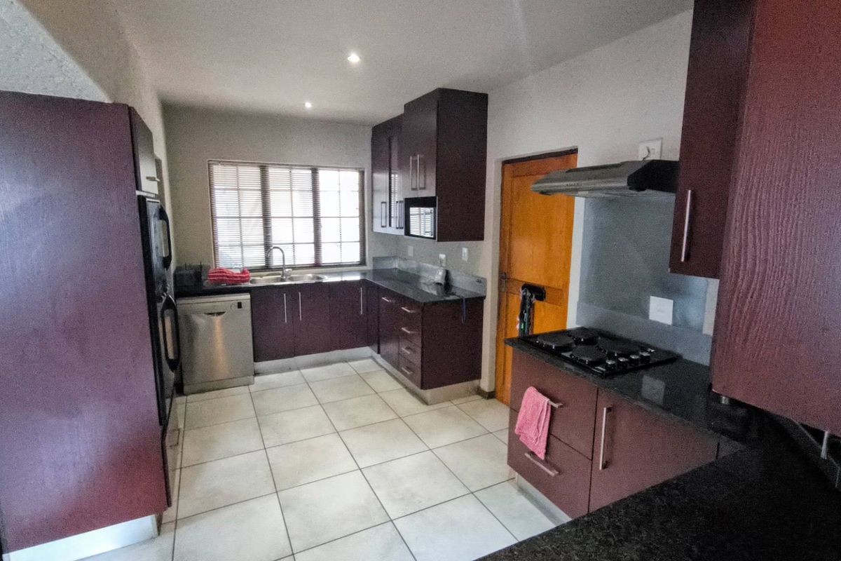 A functional kitchen featuring dark cabinetry, granite countertops, a built-in gas hob, extractor fan, and tiled flooring.