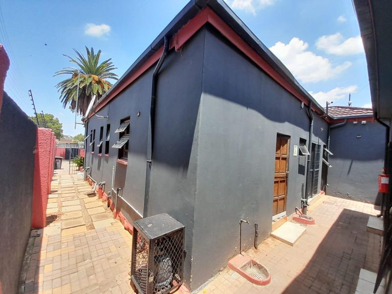 Rear exterior view of the property featuring paved pathways, dark painted walls, and functional security features including a gate and window awnings.