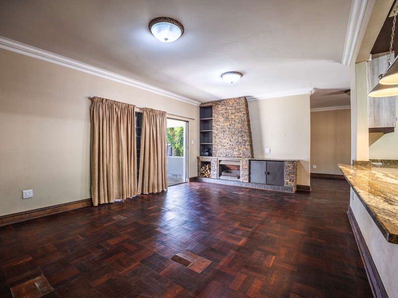 Spacious open-plan living area featuring dark parquet flooring, a stone-clad fireplace with built-in shelving, and direct access to the patio through sliding doors.