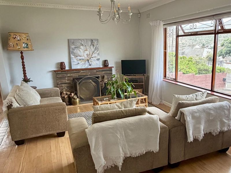 A cozy living room featuring a stone fireplace, hardwood flooring, and large windows that provide natural light and exterior views.