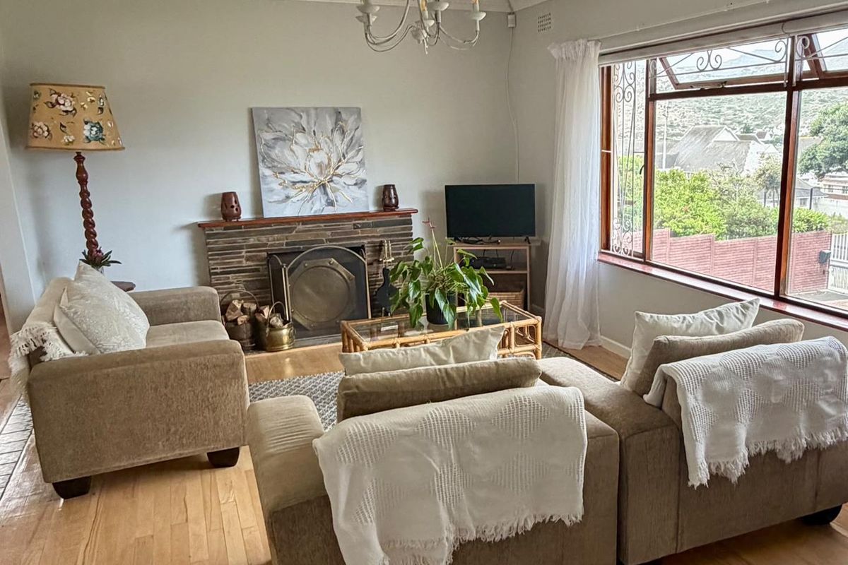 A cozy living room featuring a stone fireplace, hardwood flooring, and large windows that provide natural light and exterior views.