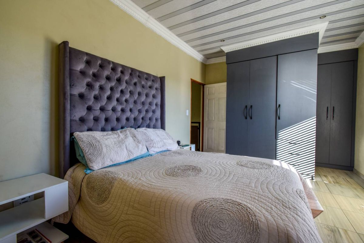 A well-maintained bedroom featuring built-in cupboards, decorative crown molding, and a unique panelled ceiling with tiled flooring.