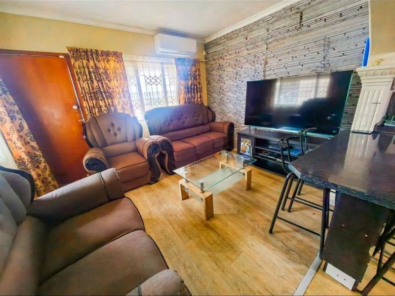 A living room featuring laminate flooring, a wall-mounted air conditioning unit, and security bars on the window.