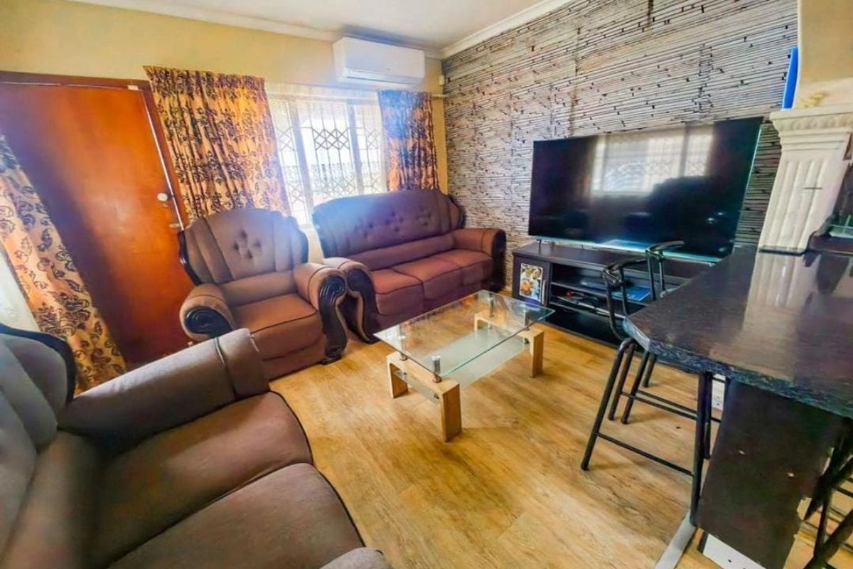 A living room featuring laminate flooring, a wall-mounted air conditioning unit, and security bars on the window.