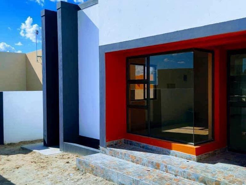 Modern front facade featuring a bold red accent wall, large bay window, and tiled entrance steps, currently awaiting final landscaping.