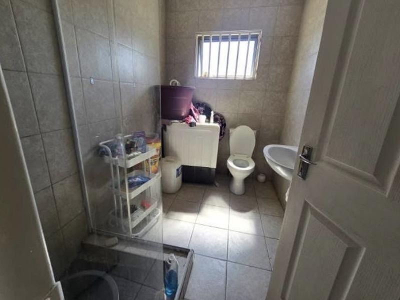 A functional bathroom featuring a shower enclosure, toilet, and pedestal basin with tiled finishes and a window with security bars.