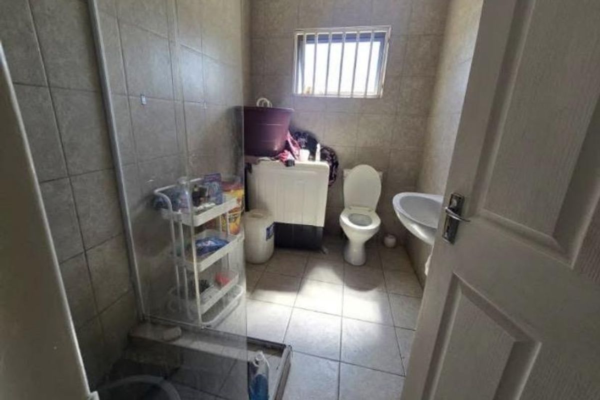 A functional bathroom featuring a shower enclosure, toilet, and pedestal basin with tiled finishes and a window with security bars.