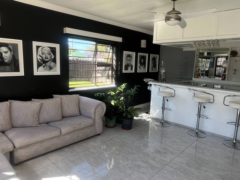 A well-appointed entertainment bar area featuring a built-in counter, mirrored backsplash, glass shelving, ceiling fan, and polished tiled flooring.