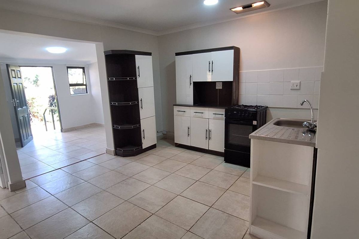 A functional kitchen area featuring tiled flooring, built-in cabinetry, a freestanding stove, and a stainless steel sink, with an adjacent open-plan living space.