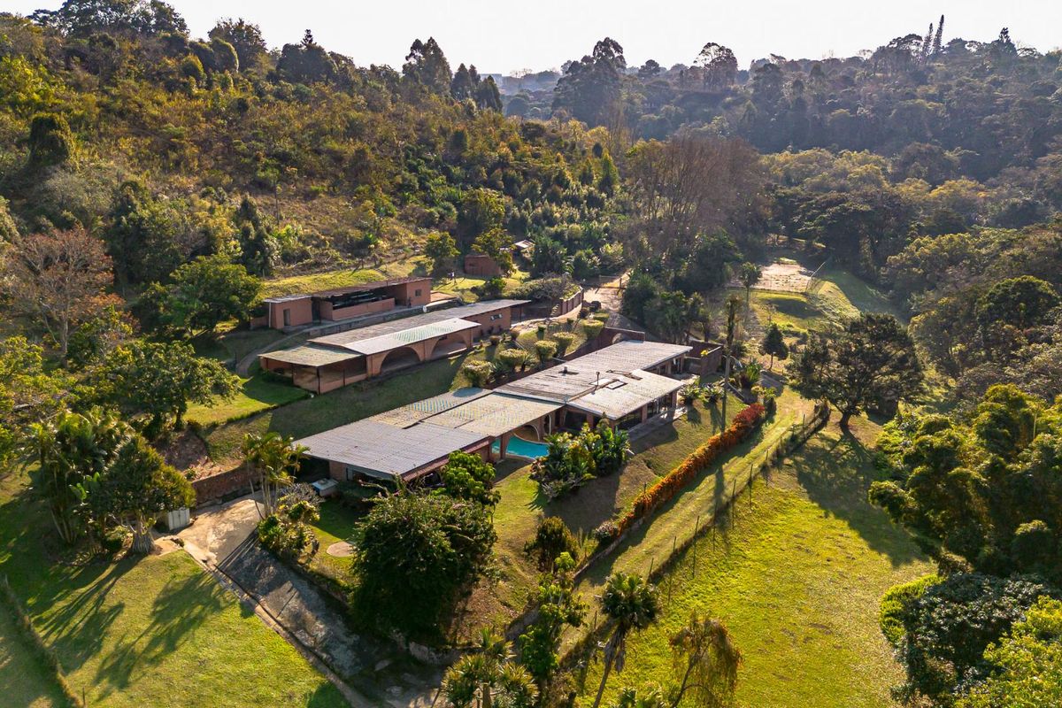 Aerial view of a sprawling property featuring multiple structures, a swimming pool, and extensive landscaped grounds set within a natural, wooded environment.