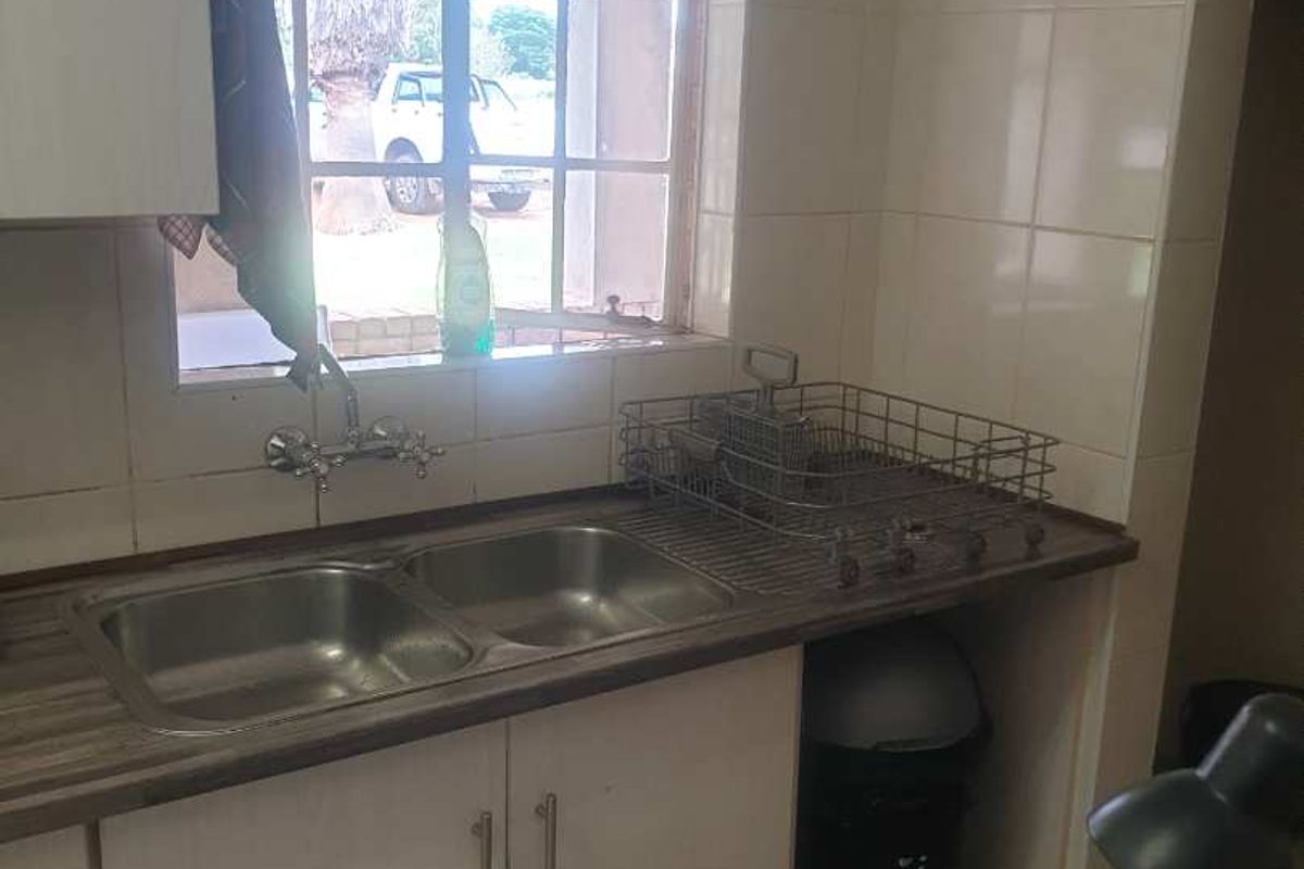 A functional kitchen area featuring a double basin sink, laminate countertops, and tiled splashbacks with natural light from a window.