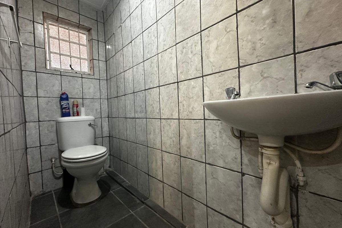 A compact bathroom featuring floor-to-ceiling tiled walls, a standard pedestal basin, and a toilet, requiring cosmetic updates to modernize the space.