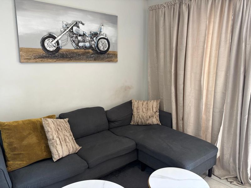 A living room area featuring neutral wall finishes and floor-to-ceiling curtains, showing minor signs of wall surface wear.