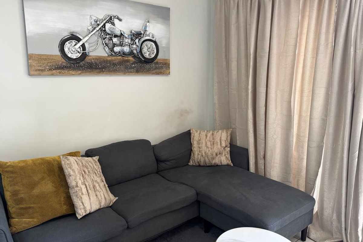 A living room area featuring neutral wall finishes and floor-to-ceiling curtains, showing minor signs of wall surface wear.