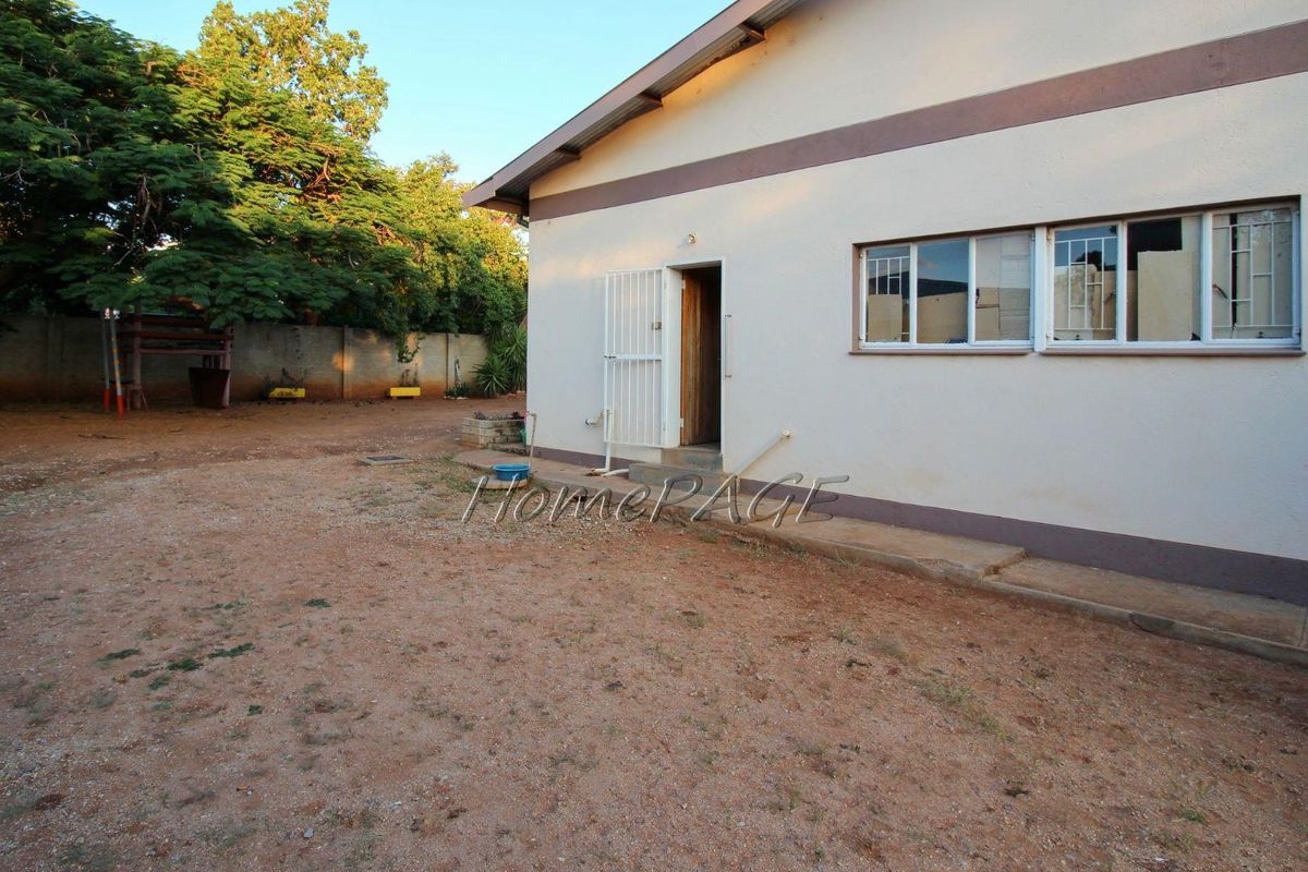 Rear view of the property showing the exterior wall, metal security gate, and a large, unpaved backyard area.