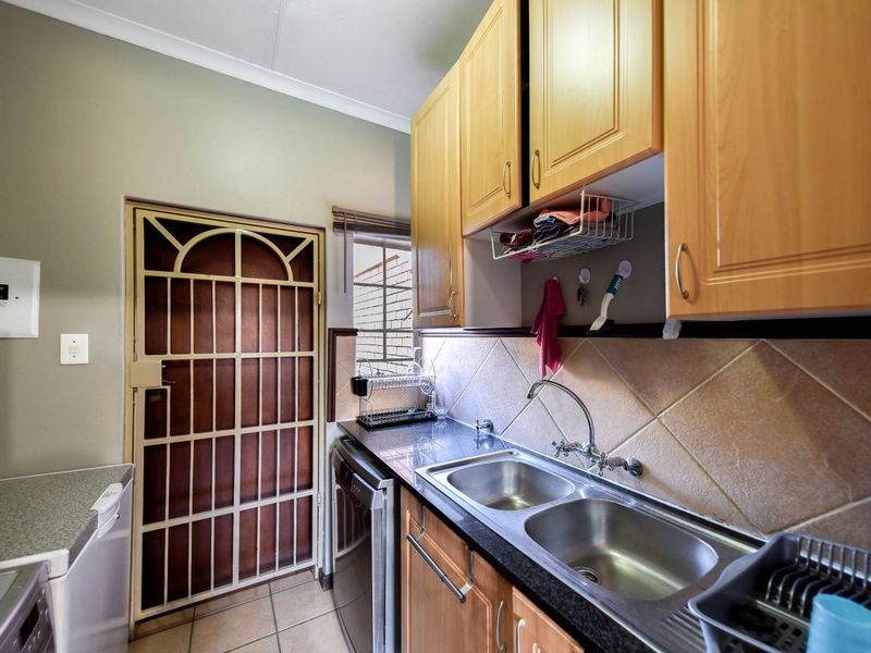 Functional scullery area featuring double bowl stainless steel sink, granite countertops, tiled splashback, and ample wooden cabinetry with an integrated security door.