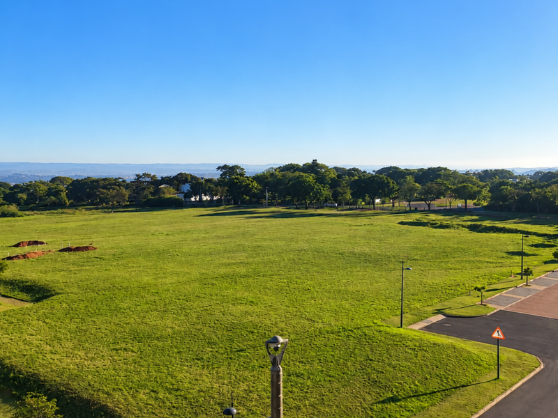 An elevated view overlooking a large open green space, paved roads, and surrounding trees under a clear blue sky.