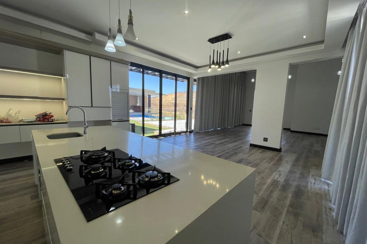Spacious open-plan kitchen and living area featuring a modern island with gas cooktop, sleek cabinetry, and large sliding doors leading to the outdoor space.