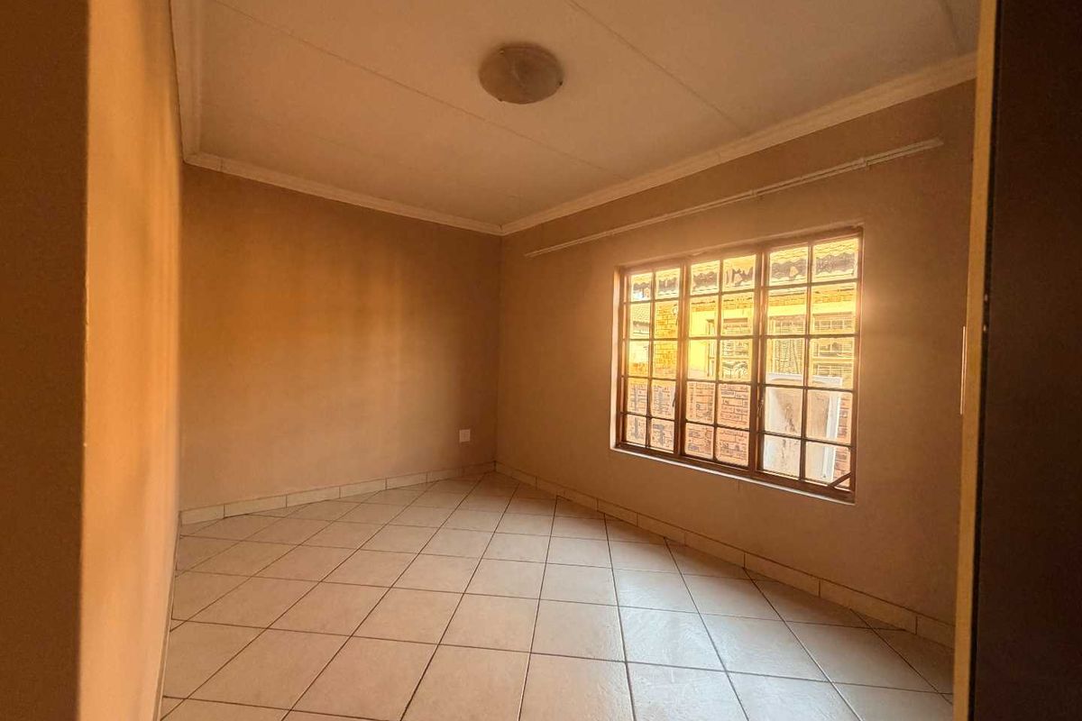 An empty bedroom featuring tiled flooring and a window fitted with security burglar bars, offering a blank canvas for potential interior design updates.