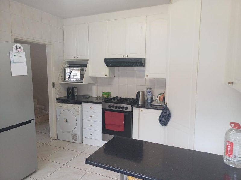 Functional kitchen featuring white cabinetry, black granite countertops, gas hob, oven, extractor fan, and tiled flooring with a convenient adjacent laundry area.