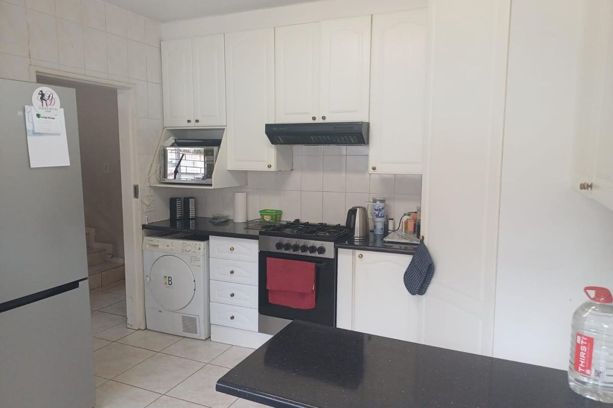 Functional kitchen featuring white cabinetry, black granite countertops, gas hob, oven, extractor fan, and tiled flooring with a convenient adjacent laundry area.