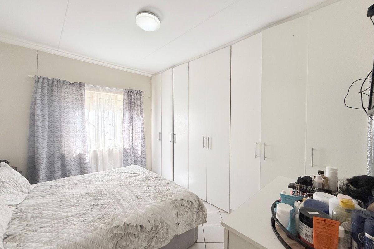 A functional bedroom featuring extensive white built-in cupboards, tiled flooring, and natural light from the window.