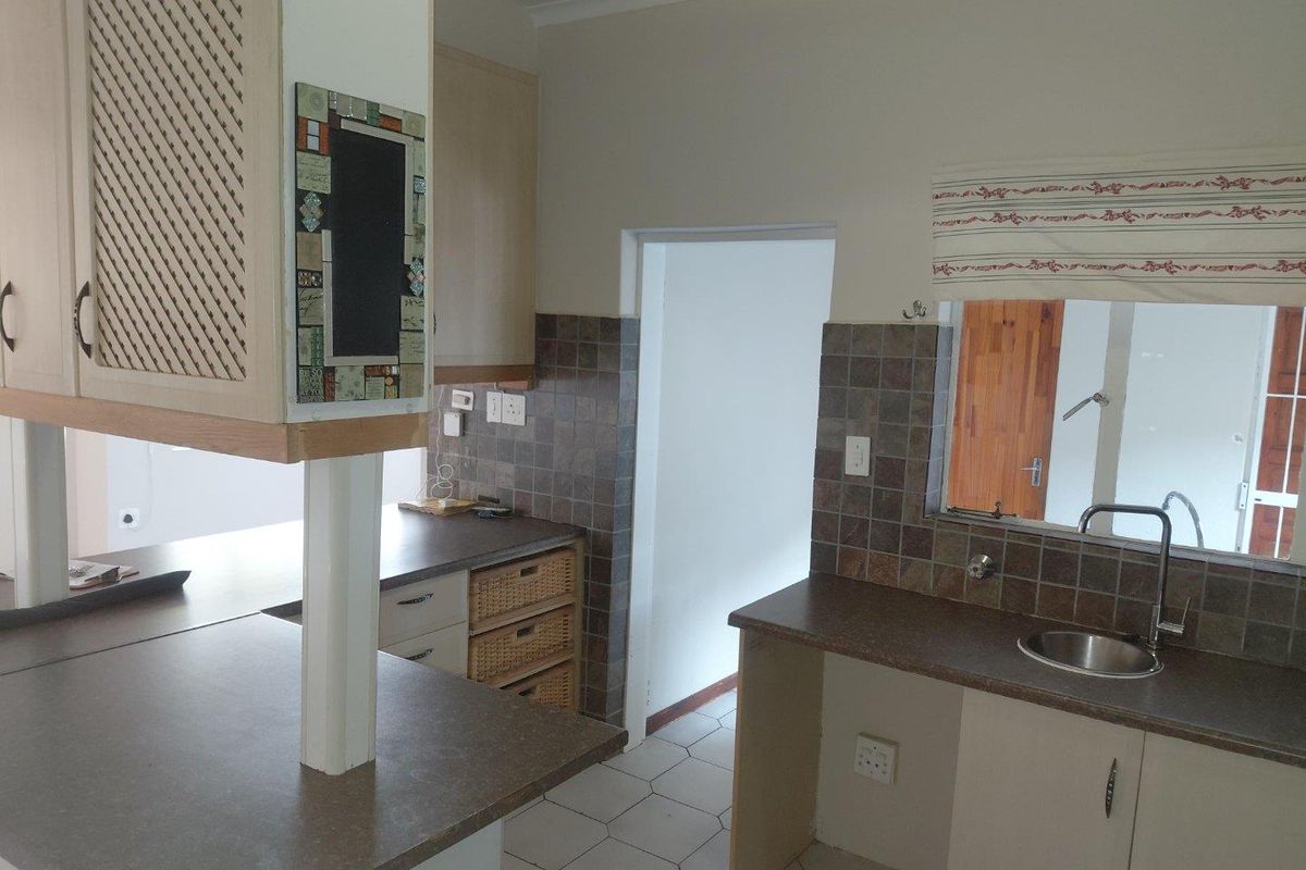 A functional kitchen featuring laminate countertops, tiled backsplash, built-in cabinetry, and a stainless steel sink with a mixer tap.