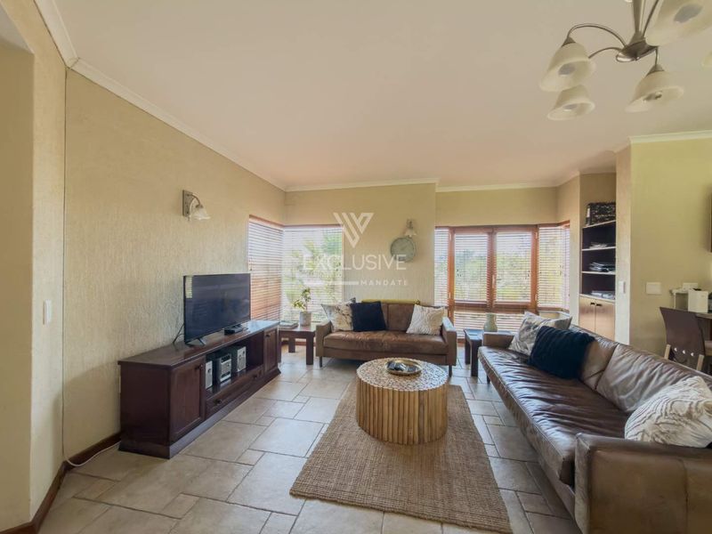 A comfortable living room featuring tiled flooring, built-in shelving, and large windows with venetian blinds, offering a functional and well-lit space.