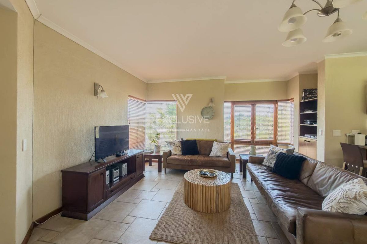 A comfortable living room featuring tiled flooring, built-in shelving, and large windows with venetian blinds, offering a functional and well-lit space.