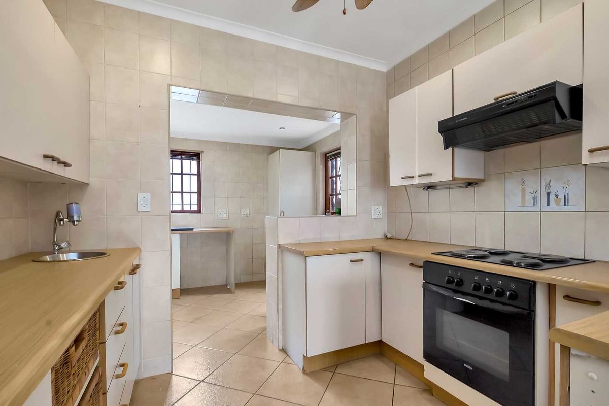 A functional kitchen featuring light-toned cabinetry, laminate countertops, a built-in oven, and an extractor fan, with an open-plan layout connecting to an adjacent utility area.